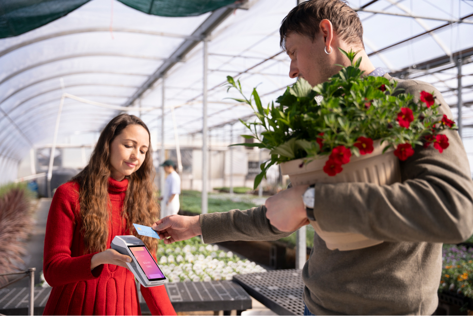 A person making a contactless payment to purchase flowers with a payment card on a Helcim credit card machine