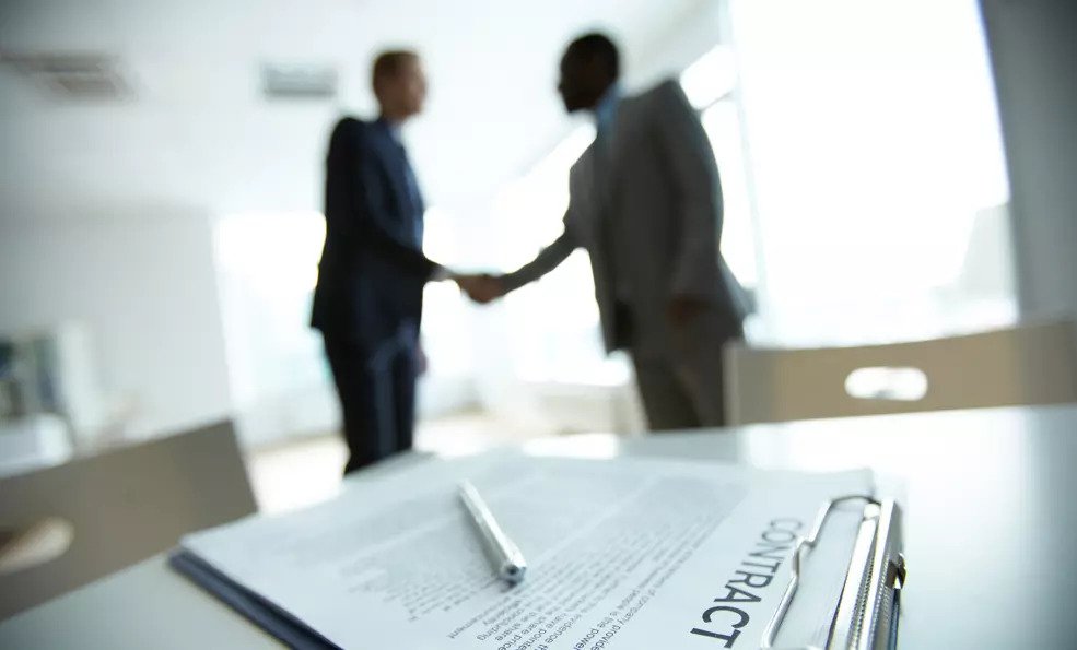two individuals shaking hands in behind a contract