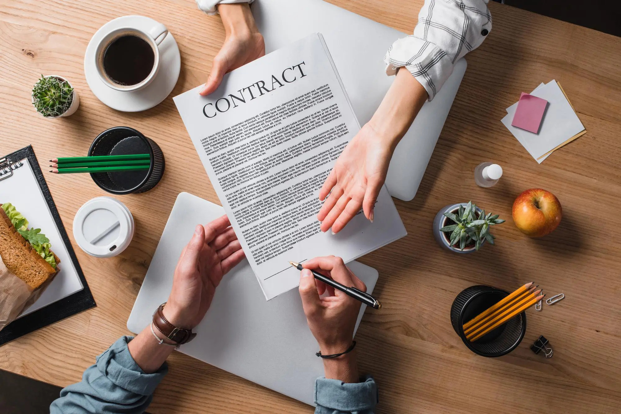 table with assorted items and two people passing a contract back and forth