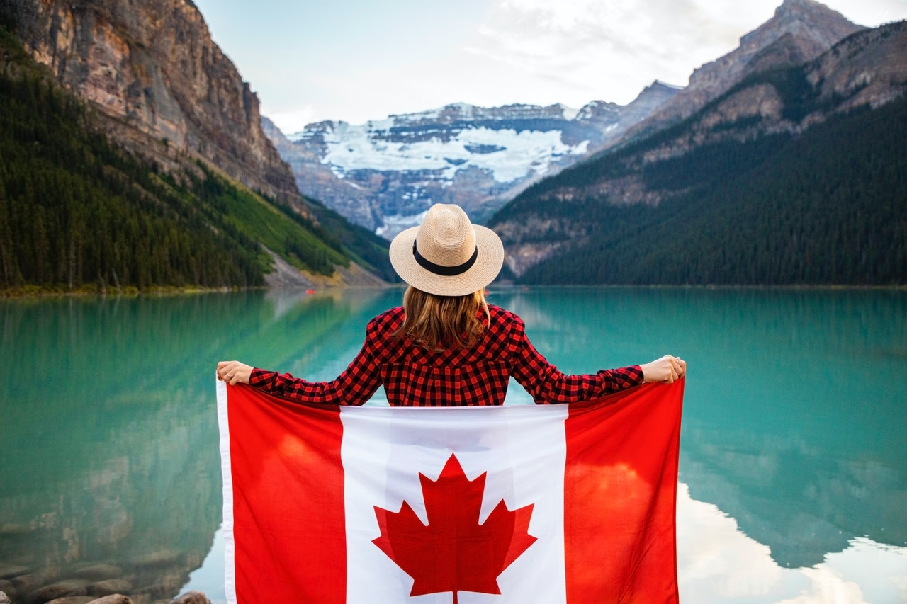 person standing in front of a lake holding a Canadian flag