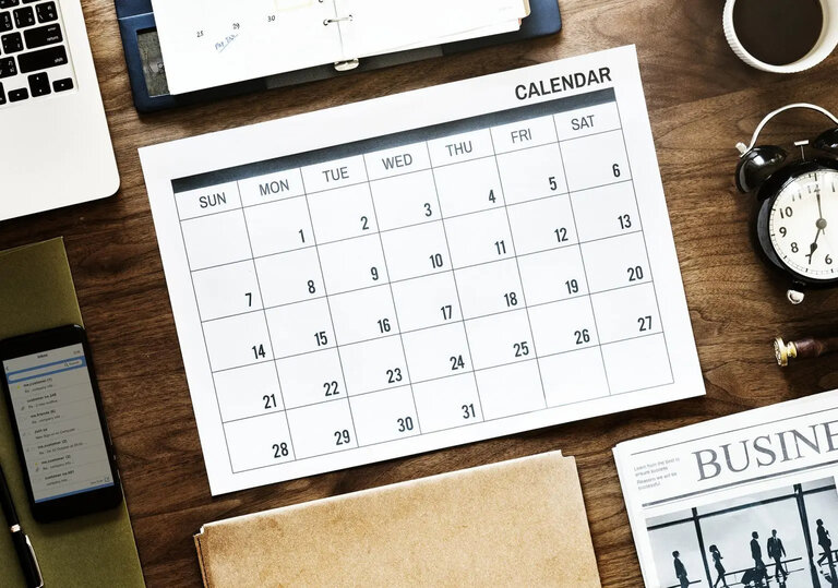 A calendar on a desk with coffee a phone and a laptop